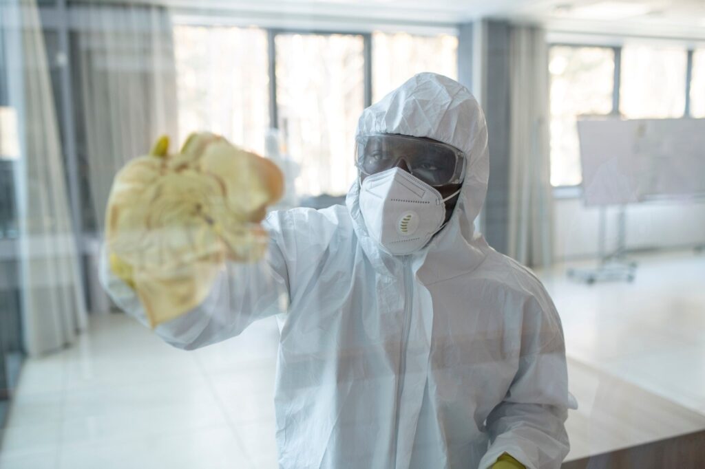 Industrial Cleaning Services 4 - CleanPro of America Person in full protective PPE (suit, mask, goggles) extends a yellow-gloved hand toward the camera holding a yellow cloth area visible at the edge of the frame.